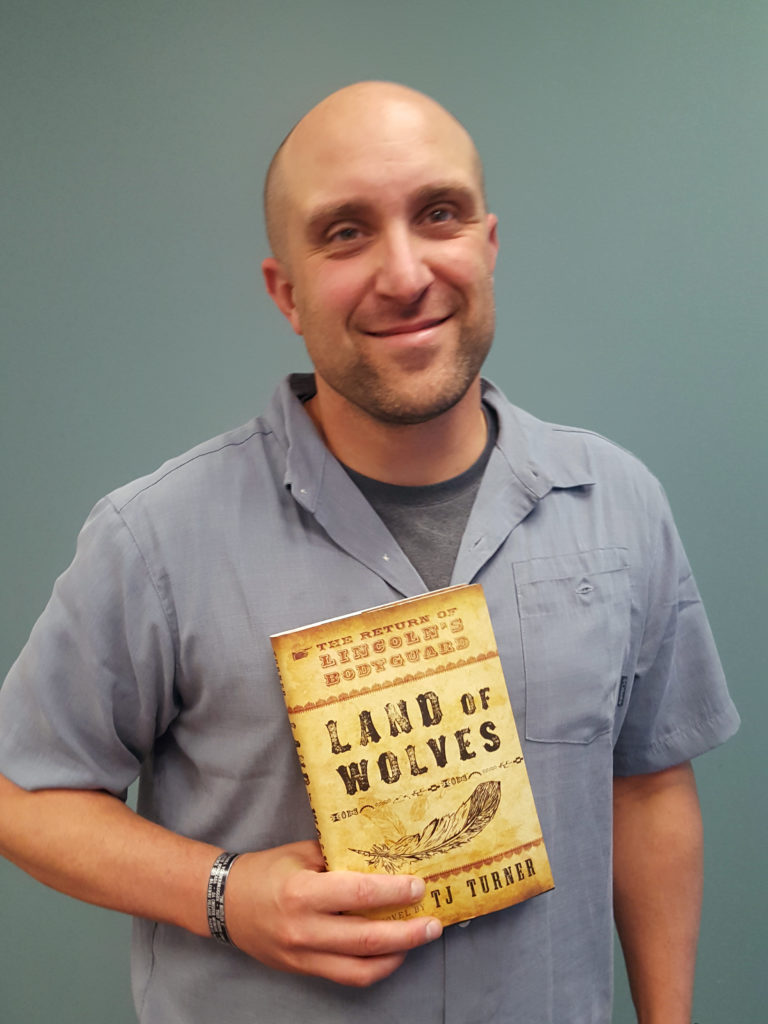 Author TJ Turner holding a copy of his novel, "Land of Wolves".